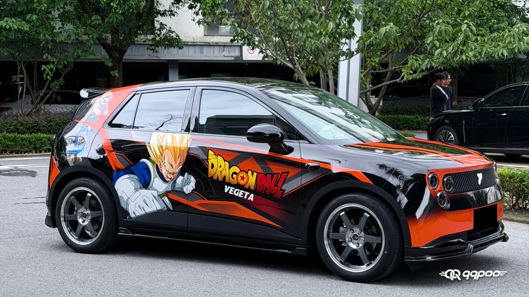 Front three-quarter view of a black car with a Dragon Ball Z Vegeta car wrap and orange-red graphics.